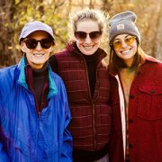 Three women stand smiling together in fall weather.