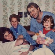 A family photo of a woman who just had a baby in the hospital and two other children and her husband surround her.