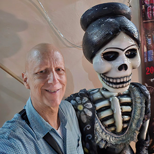 Man smiles with skeleton statue wearing a blue shirt with a collar
